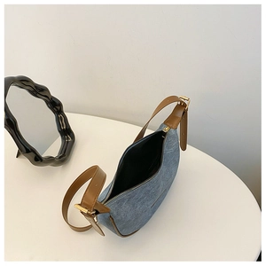 Top view of denim hobo bag with brown leather strap and gold buckle on white table