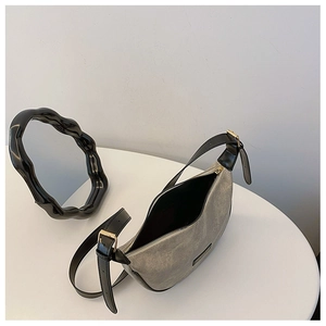 Detail of grey crescent bag with leather trim and adjustable strap on white table