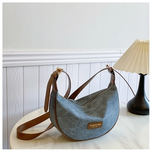 Detail of grey felt dumpling bag with brown leather trim and golden hardware on marble