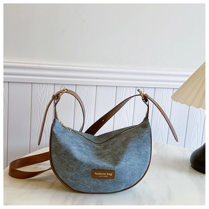 Detail of blue denim crescent bag with brown leather trim on white marble surface