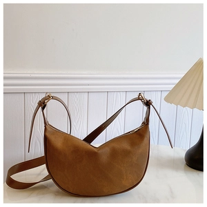 Detail of a brown suede hobo bag with gold zipper and adjustable metal buckle strap