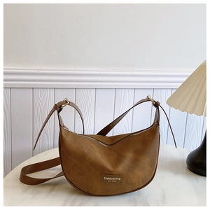 Detail of a brown crescent-shaped bag with a leather label and an adjustable strap