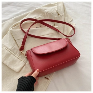 Detail view of a red matte leather crossbody bag styled on a white blazer background