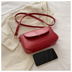 Close-up of red vegan leather crossbody bag with gold hardware placed on a beige blazer