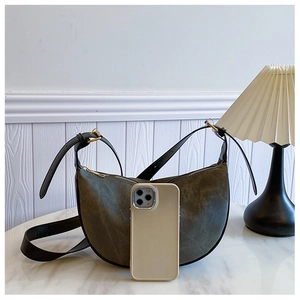 Detail of a dark green crescent dumpling bag with matte gold hardware and leather strap