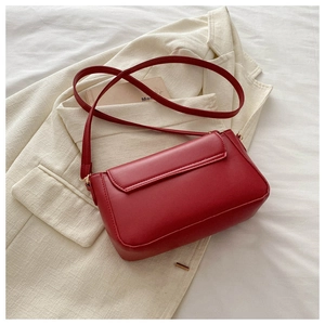 Detail of red faux leather flap bag placed on white fabric and cream suit jacket