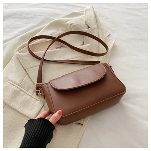 Close-up of brown matte leather crossbody bag with rounded flap and adjustable strap