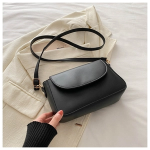 Close-up of a black leather crossbody bag with gold metal buckle and smooth flap design