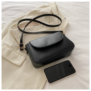 Top view of a black leather mini square bag with adjustable strap over a beige blazer
