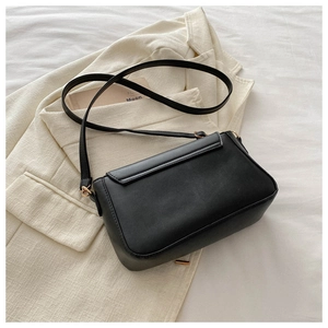 Close-up of black matte square crossbody bag with gold hardware on beige blazer