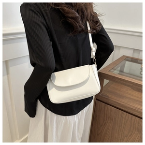 Close-up of a white minimalist shoulder bag with gold hardware worn in a lifestyle setting
