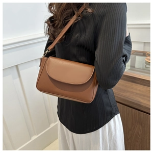 Brown leather crossbody bag with gold buckle shown worn over shoulder on a model