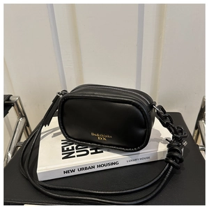 Close-up of black crossbody bag with golden logo, metal zipper and thick chain detail