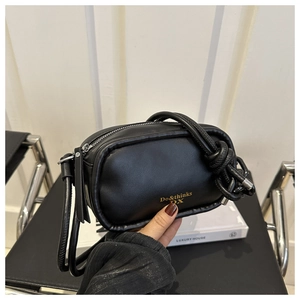 Close-up of a black leather handbag featuring a knotted shoulder strap and gold logo