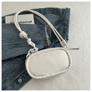 White oval PU crossbody bag with thick chain detail on blue denim and book
