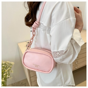 Pink oval leather shoulder bag with chain strap shown in a cozy indoor lifestyle setting