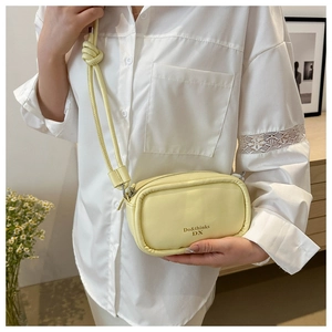 Close-up of pale yellow leather crossbody bag with knot strap and brand logo detail