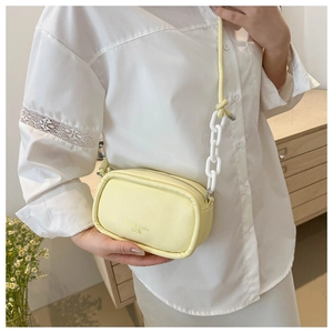 Detail of a pale yellow crossbody bag with a white chunky chain and a slim leather strap