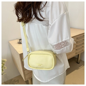 Detail view of a pale yellow crossbody bag with gold lettering and a slim shoulder strap