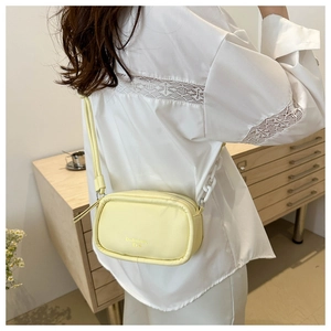 Detail of light yellow crossbody camera bag with zipper and decorative chain strap