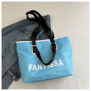 Detail of light blue Oxford tote bag featuring white FANYISSA text and black nylon straps