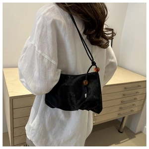 Detalle de bolso bandolera negro plisado con cuentas de ámbar y acabado brillante