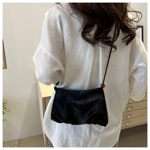 Détail du sac bandoulière noir plissé avec une perle ambrée sur la bandoulière