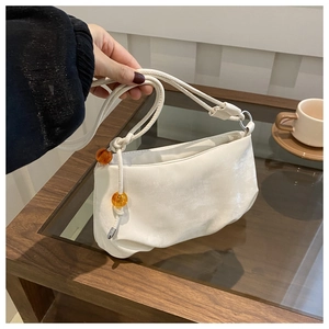 Détail d'un sac crème avec perles ambrées et bandoulière à nœuds sur table en bois