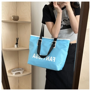 Detailed close-up of blue nylon tote bag showing white letter print and black shoulder strap