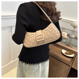 Sac baguette beige matelassé avec grande boucle porté à l'épaule dans un décor moderne