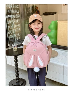 Pink student backpack with rabbit ears and plush tail shown on a young girl in a cafe