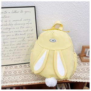 Detail of yellow rabbit ears backpack with a white pom-pom tail on a wooden shelf