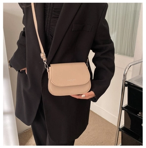 Détail d'un petit sac bandoulière beige avec texte Fashion Trend porté sur un blazer noir