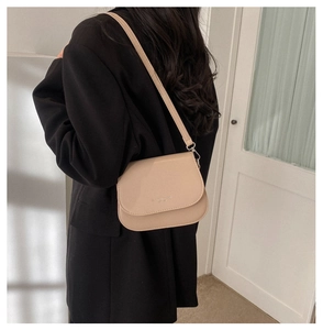 Beige minimalist saddle bag shown on model with slim shoulder strap and golden logo