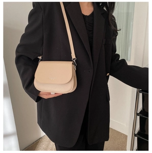 Detail of minimalist apricot saddle bag featuring a flap closure and slim shoulder strap