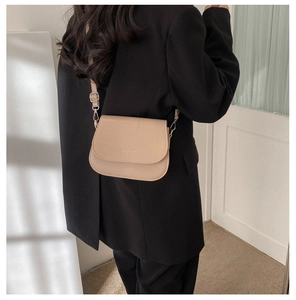Model view showing beige leather saddle bag worn crossbody over a black blazer