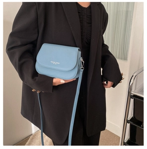 Détail du sac selle bleu clair avec lettrage blanc sur un blazer noir large