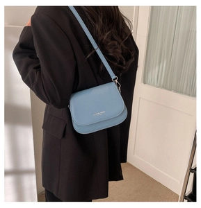 Fog blue crossbody saddle bag with gold lettering shown on model in black blazer