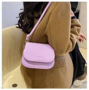 Close-up of lavender crossbody saddle bag with Fashion Trend text worn on brown coat
