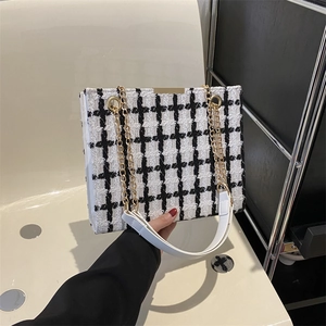 Chic black and white tweed shoulder bag with gold chain strap in a modern setting