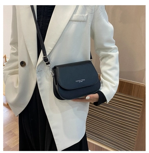Detail of black leather saddle bag with white 'FASHION TREND' text on a white blazer