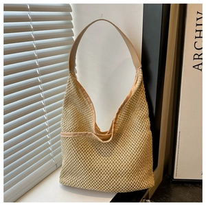 Detail of beige woven straw tote bag with smooth leather strap hanging in window light