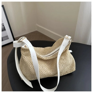 Detail of hand-woven straw tote with white leather strap and gold buckle on a black stool