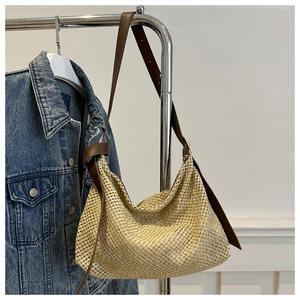 Detail of woven straw tote bag featuring brown leather straps and knotted metal ring buckle