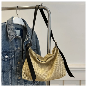 Detail of handwoven straw hobo bag featuring black knotted leather shoulder straps