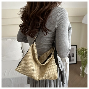 Handwoven straw tote bag with black shoulder straps shown on a model in a cozy interior