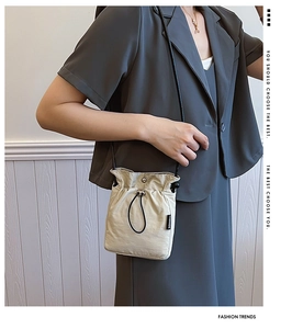 Detail of beige nylon drawstring crossbody bag with black strap and fashion label on a model