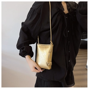 Detail of metallic gold crossbody phone bag featuring pleated leather and a woven knot
