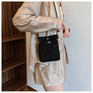 Minimalist black drawstring nylon crossbody bag worn by a model in a casual urban style