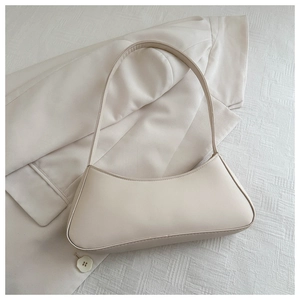 Close-up of minimalist cream white baguette bag on a textured blazer and fabric background